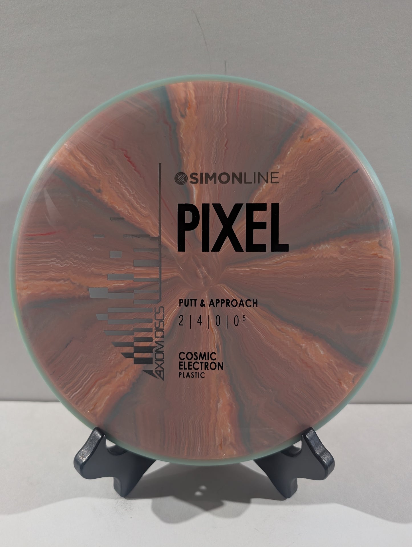 A disc golf putter and approach shot disc on a black display stand against a neutral gray background. The disc features a pink pattern with black printed text including 'SIMONLINE', 'PIXEL', and 'COSMIC ELECTRON PLASTIC'.