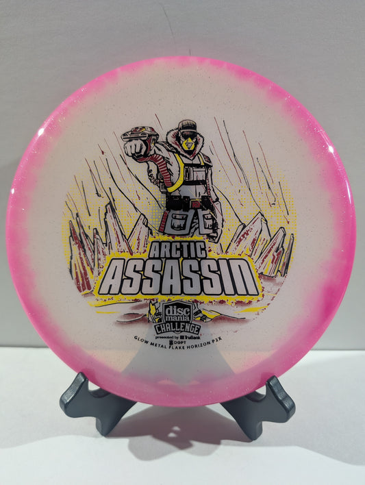A Discmania Arctic Assassin disc golf disc with a pink rim and a white center featuring a graphic of an Arctic soldier and mountains, displayed on a small stand.