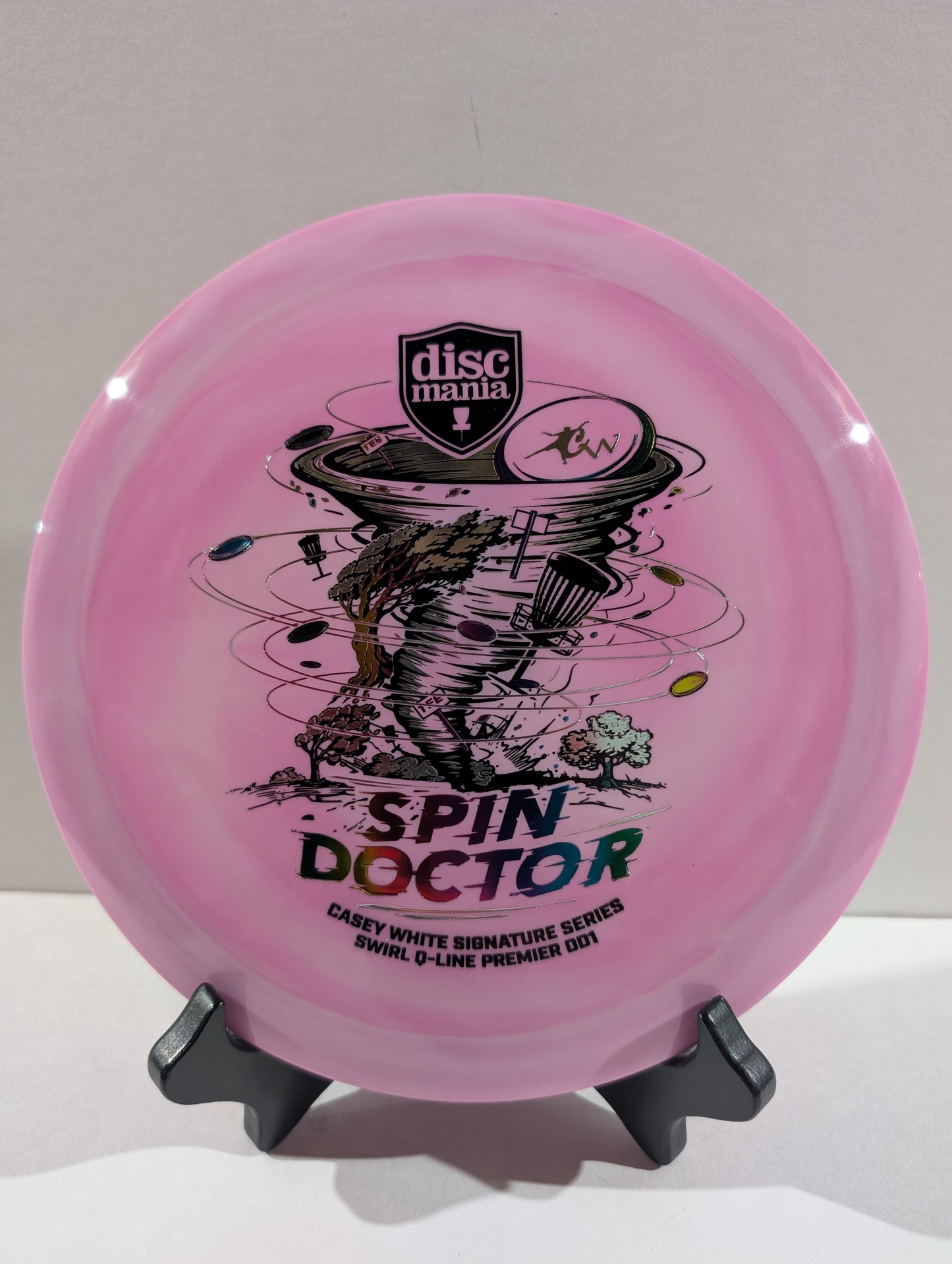 A purple Discmania 'Spin Doctor' flying disc displayed on a black stand against a neutral light gray background.