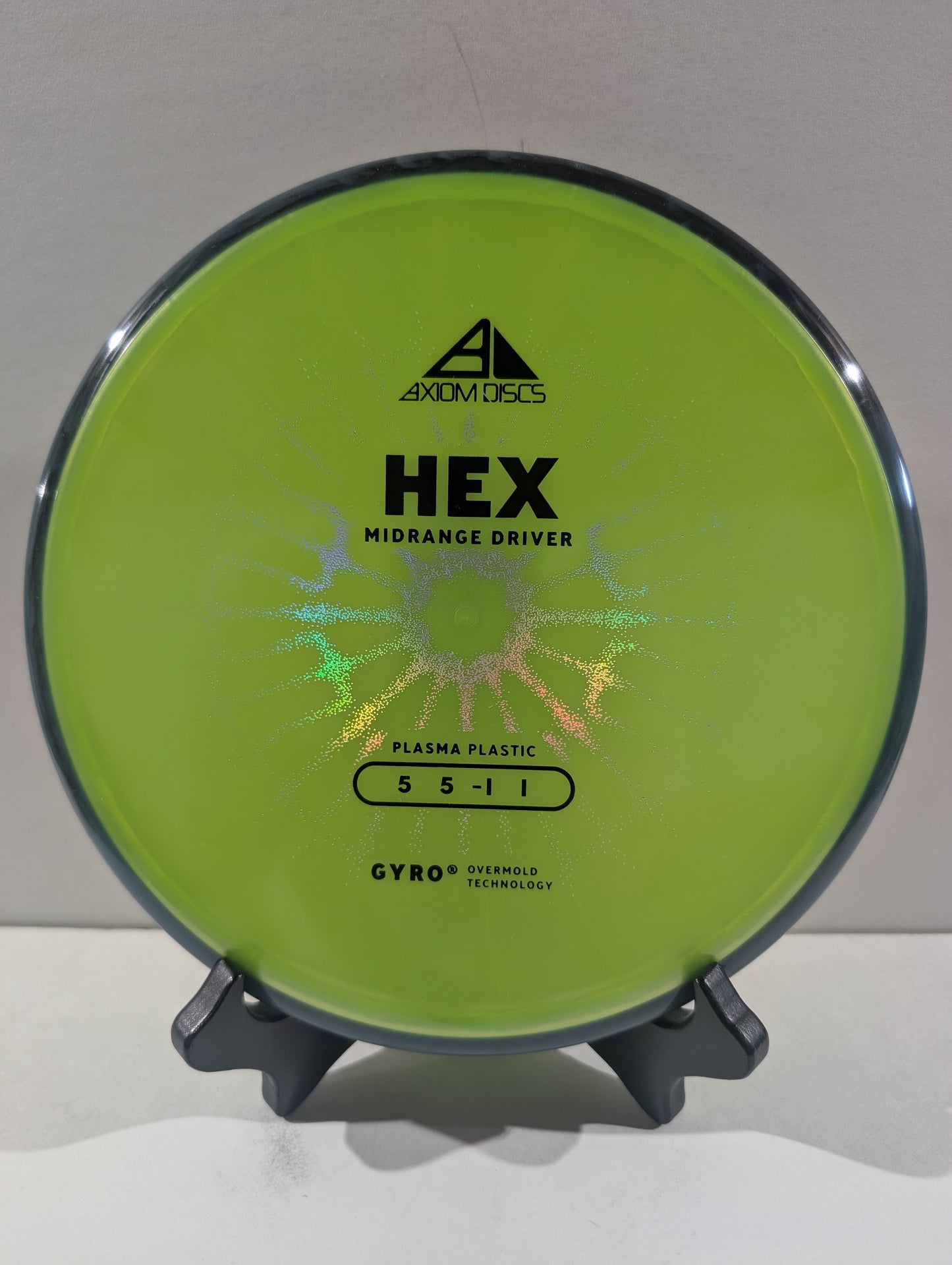 A lime green Axiom Discs Hex midrange disc golf driver displayed on a small black stand against a neutral light gray background.