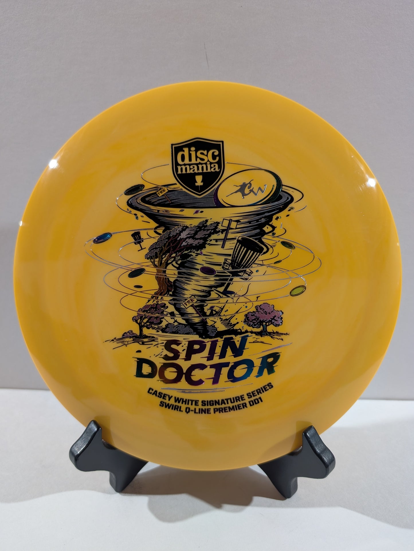 An orange Discmania 'Spin Doctor' disc golf disc displayed on a black stand against a neutral gray background.
