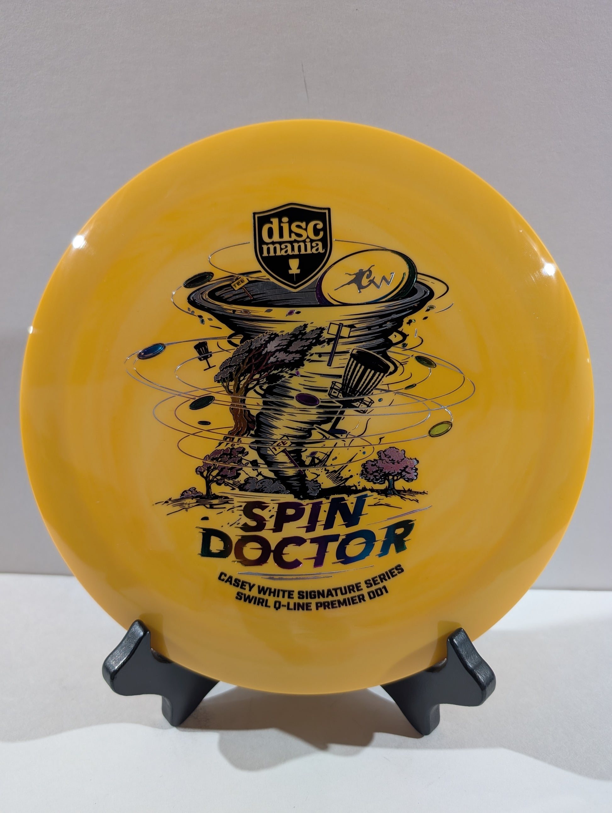 An orange Discmania 'Spin Doctor' disc golf disc displayed on a black stand against a neutral gray background.