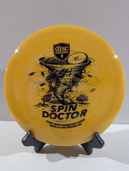 An orange Discmania 'Spin Doctor' disc golf disc displayed on a black stand against a neutral gray background.