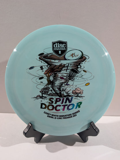 A light blue Discmania Spin Doctor disc golf disc displayed on a black stand against a neutral gray background.