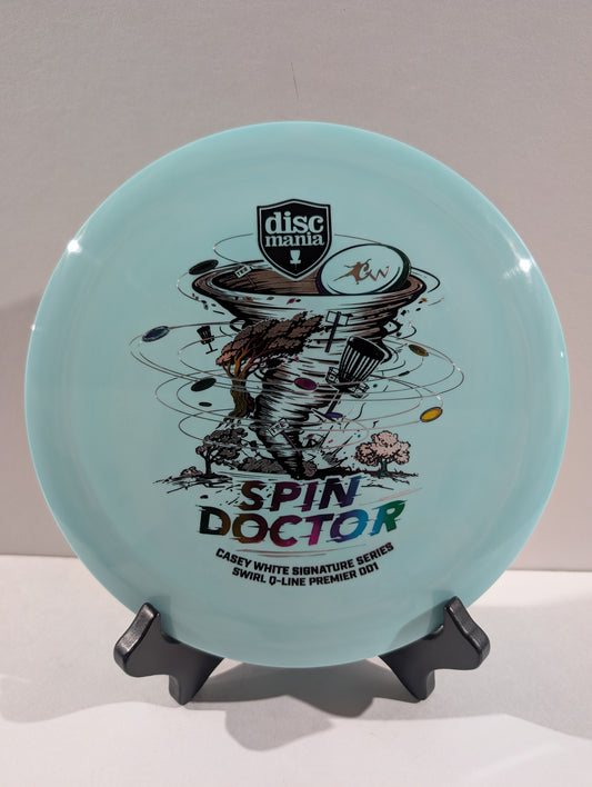 A light blue Discmania Spin Doctor disc golf disc displayed on a black stand against a neutral gray background.