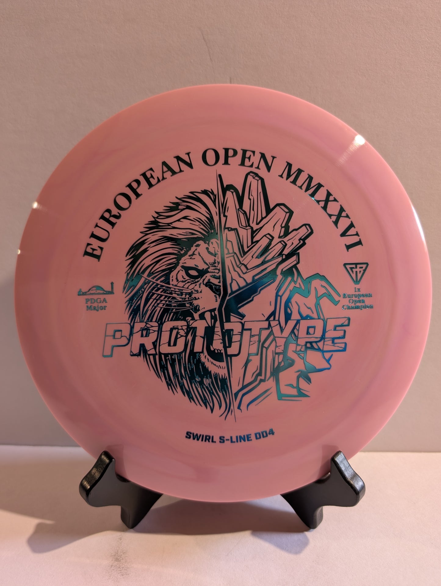 Pink disc golf disc with black graphics and text on a stand against a beige background