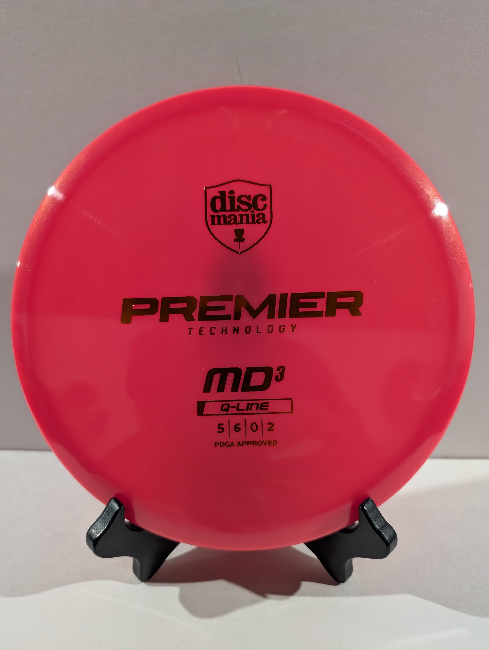 A bright pink Discmania Premier Technology MD3 disc golf disc displayed on a small black stand against a neutral gray background.