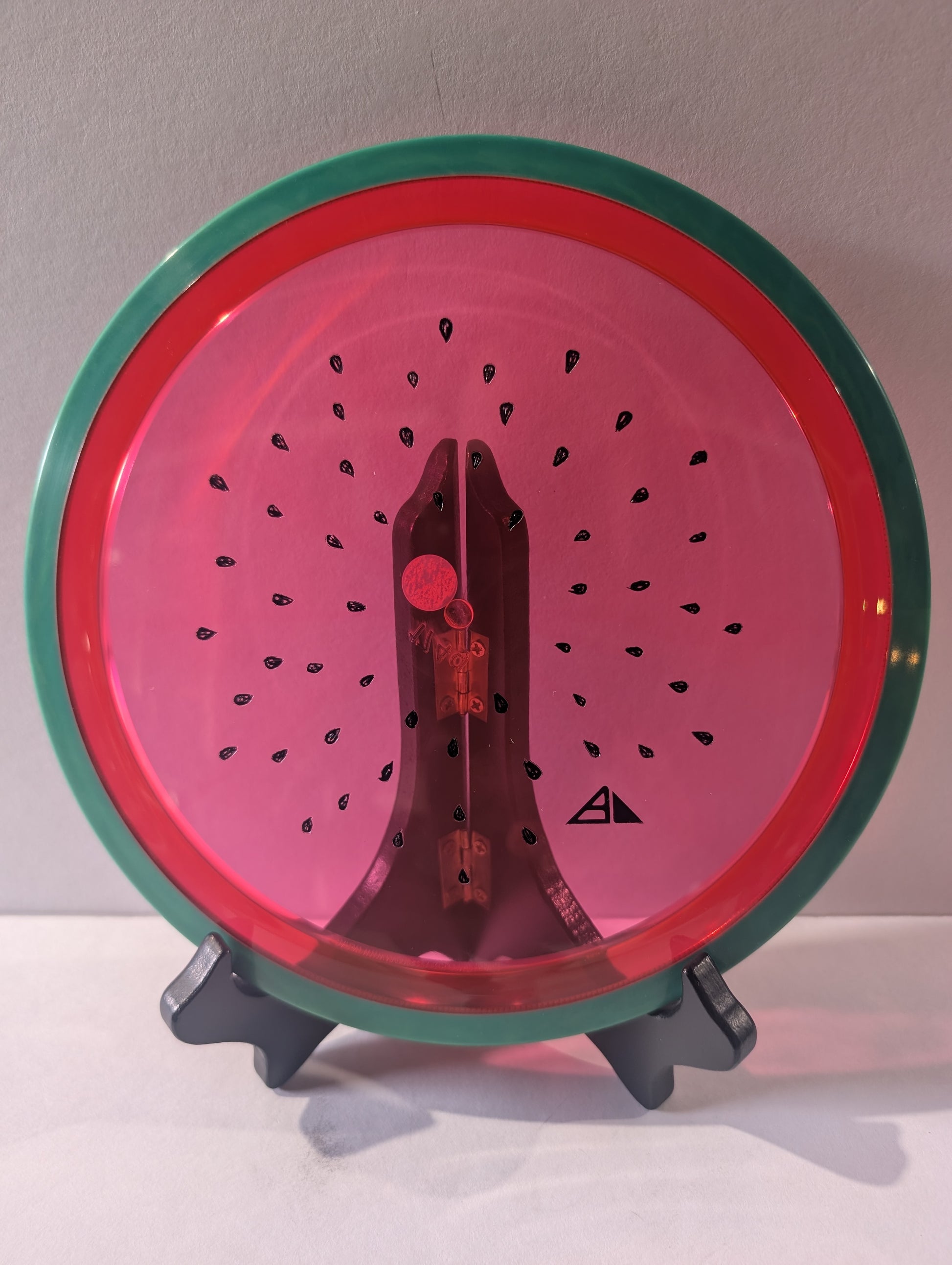 Watermelon disc colored like a watermelon with a stand on a plain background