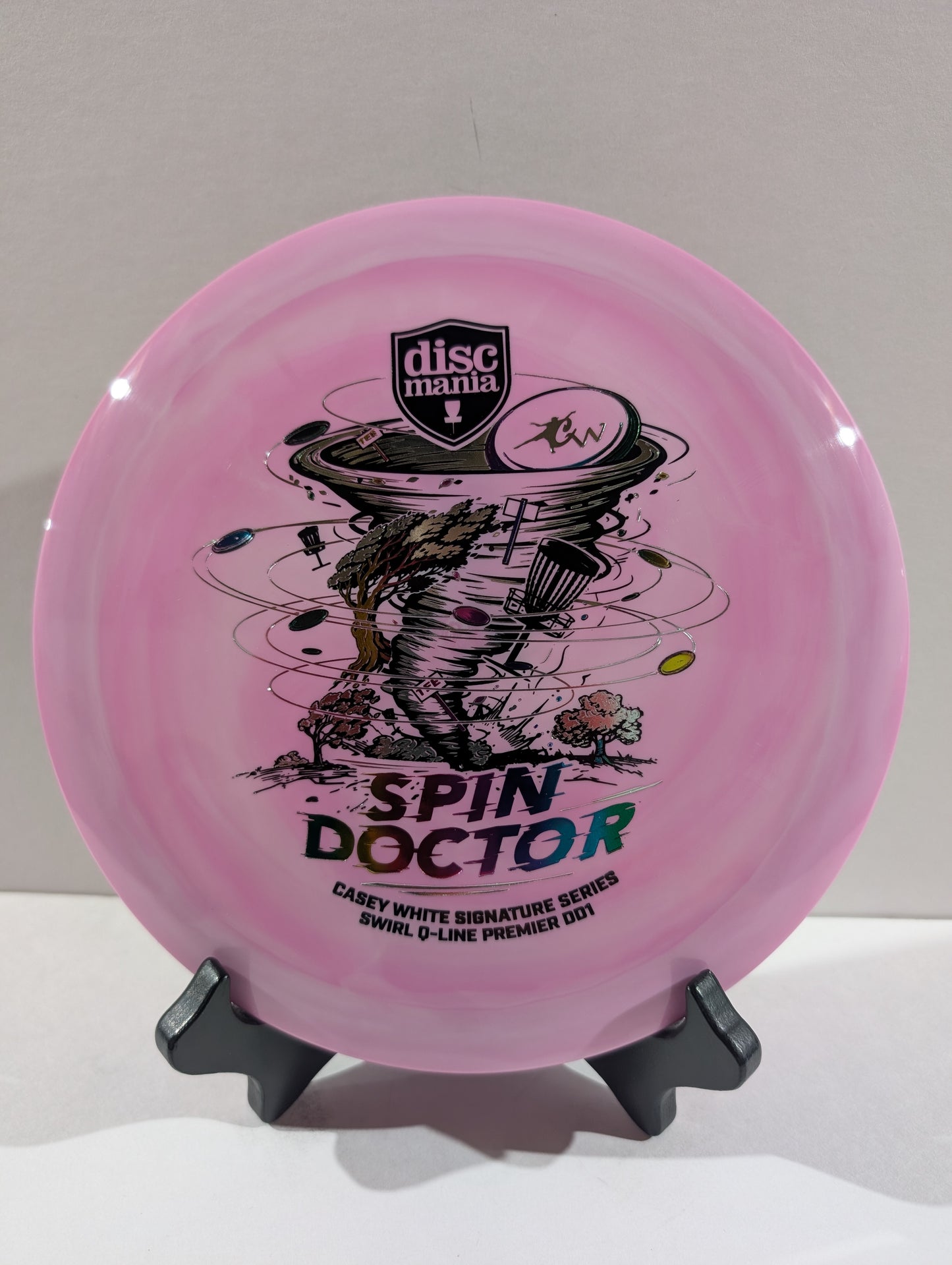 A purple Discmania 'Spin Doctor' disc golf disc displayed on a small black stand against a neutral light gray background.