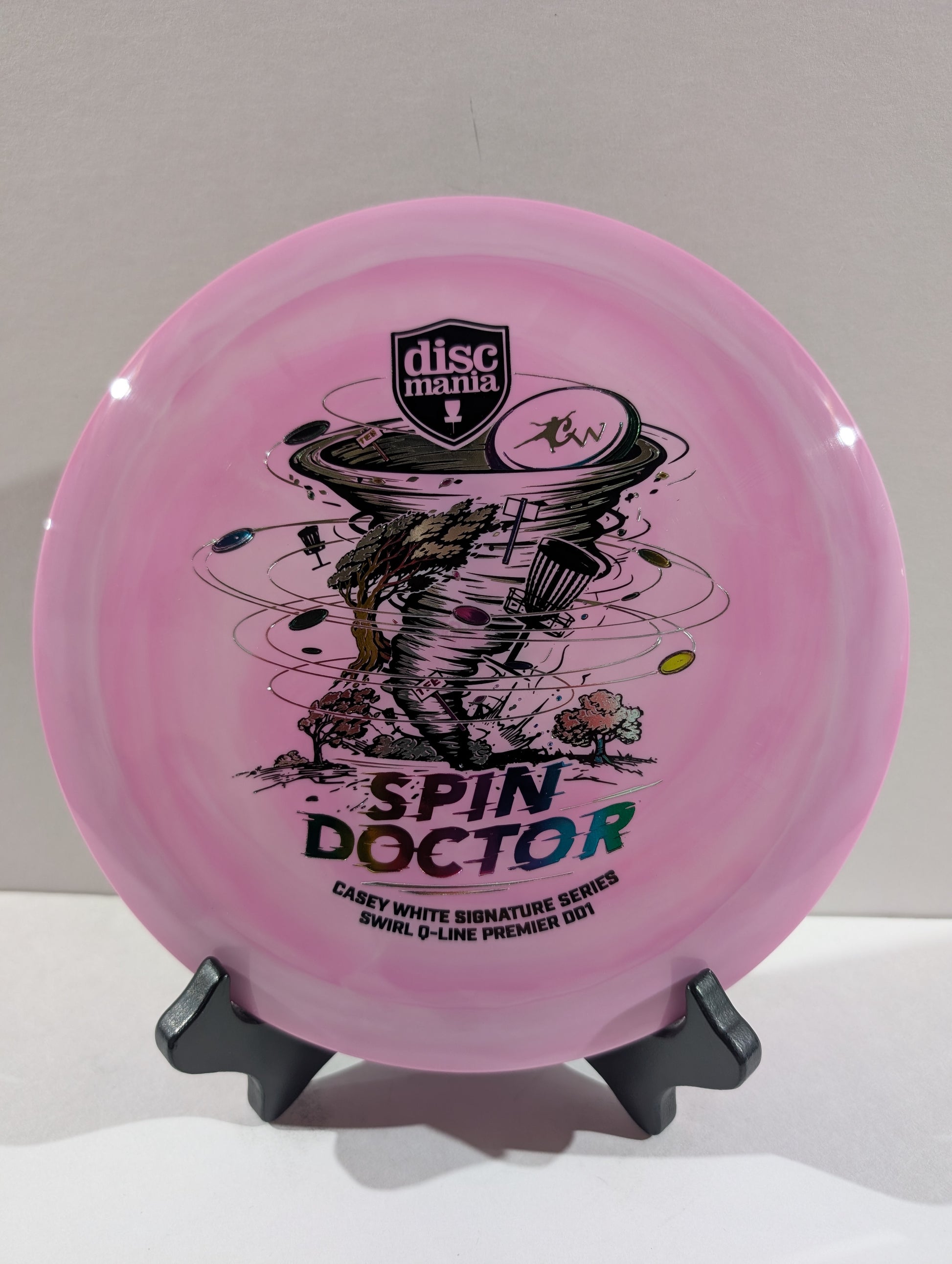 A purple Discmania 'Spin Doctor' disc golf disc displayed on a small black stand against a neutral light gray background.