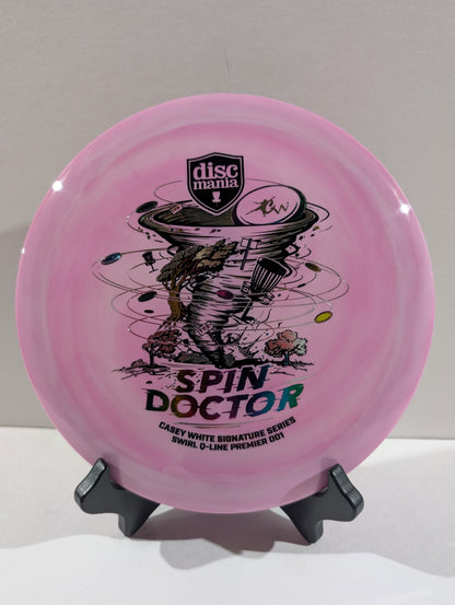 A purple Discmania 'Spin Doctor' disc golf disc displayed on a small black stand against a neutral light gray background.