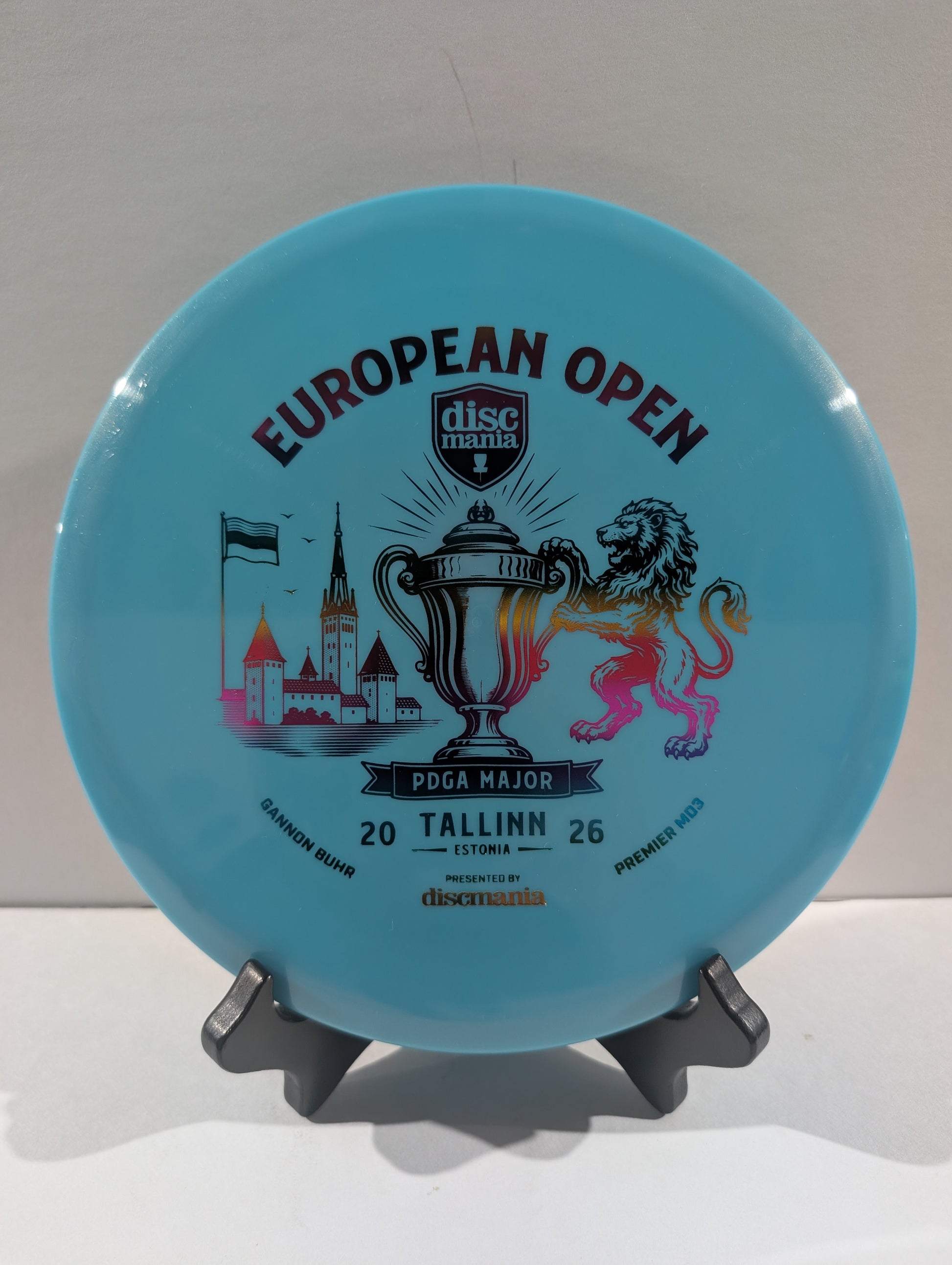 A light blue Discmania European Open disc golf disc displayed on a small black stand against a neutral light gray background.