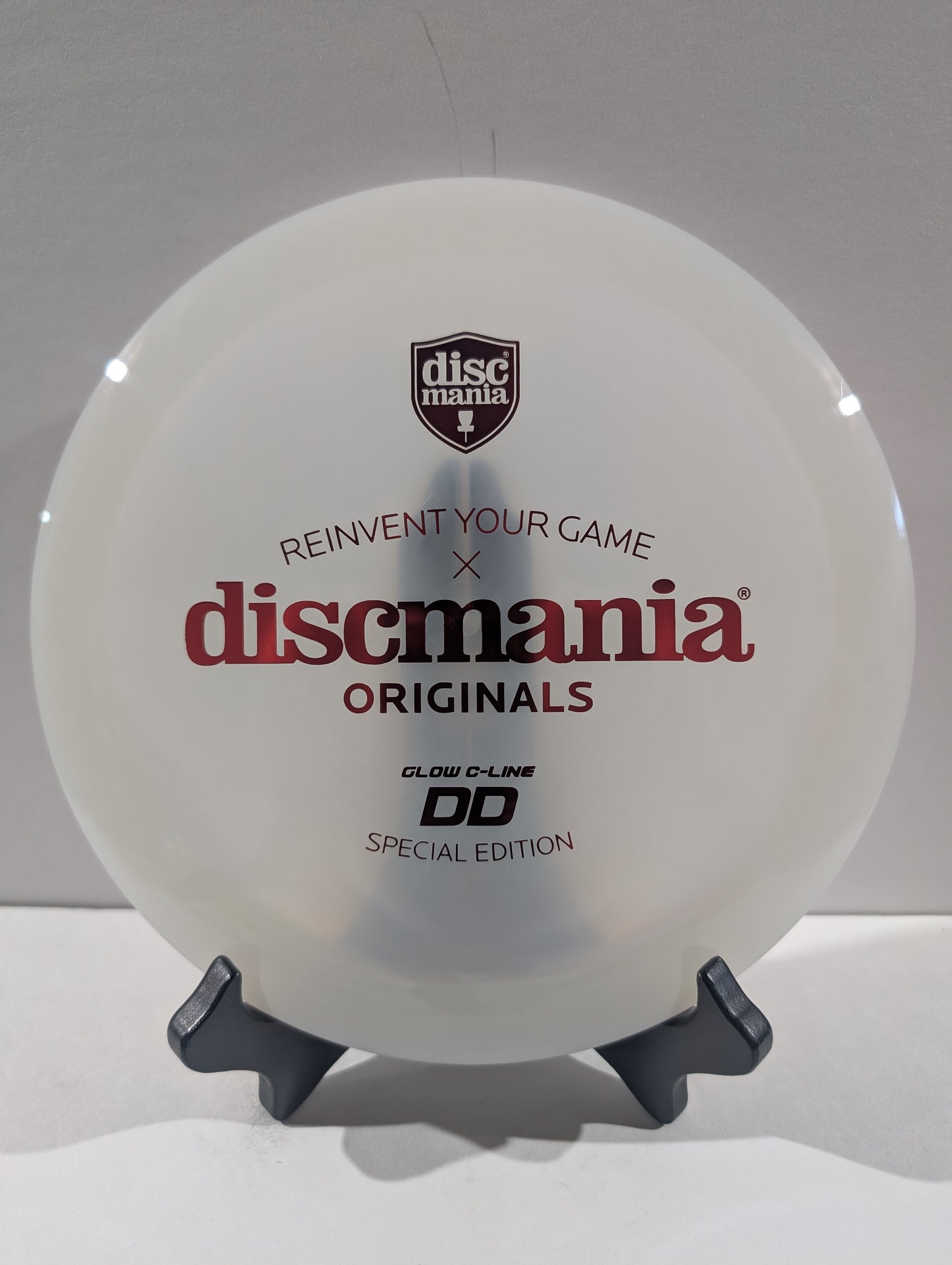 A white Discmania Originals DD Special Edition disc golf disc displayed on a small black stand against a light gray background.