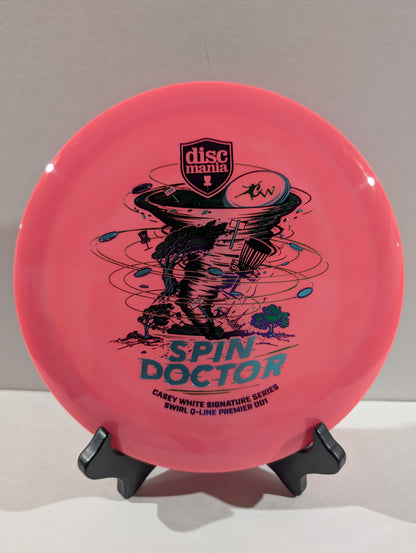 A pink Discmania Spin Doctor disc golf disc displayed on a small black stand against a neutral gray background.
