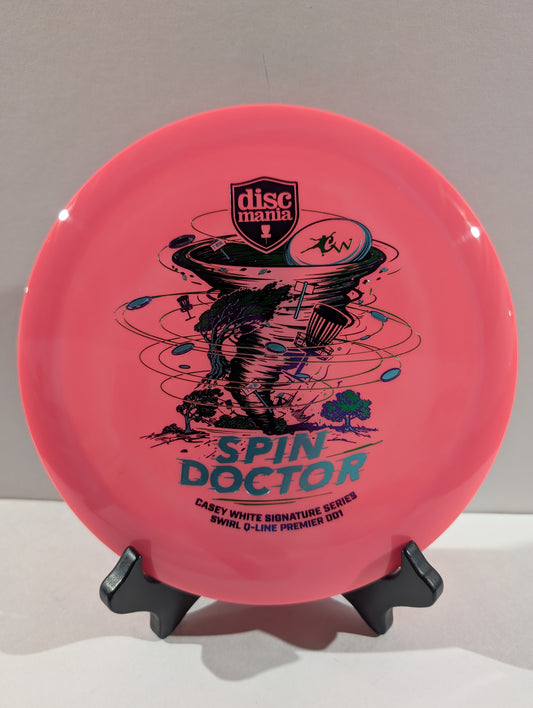 A pink Discmania Spin Doctor disc golf disc displayed on a small black stand against a neutral gray background.