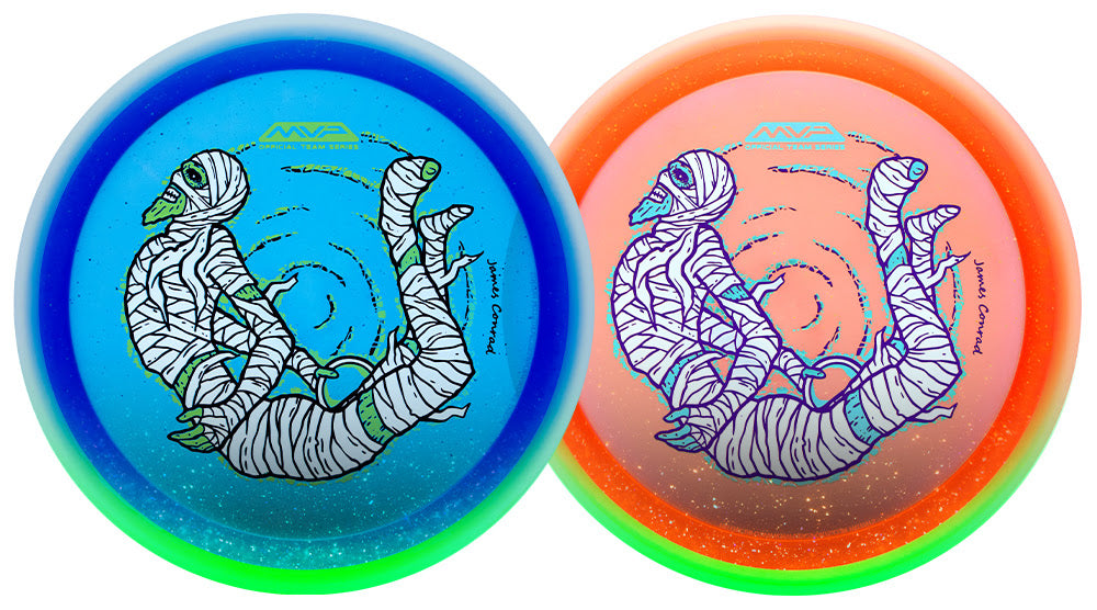 Two disc golf discs side by side, one blue with a green rim and one orange with a green rim, both featuring a white mummy illustration with green accents.